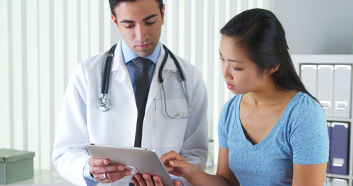 Picture of a male Physician holding a smart tablet next to a female patient that has her finger on the screen.